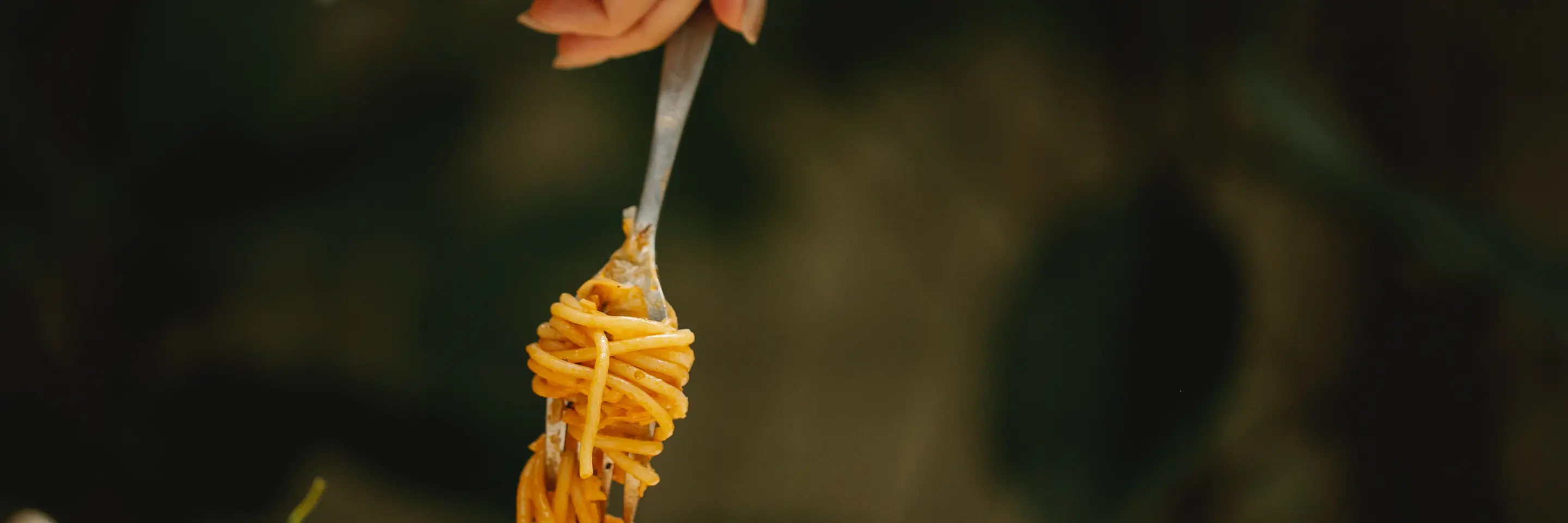 Image of a hand holding a fork with spaghetti swirled around it