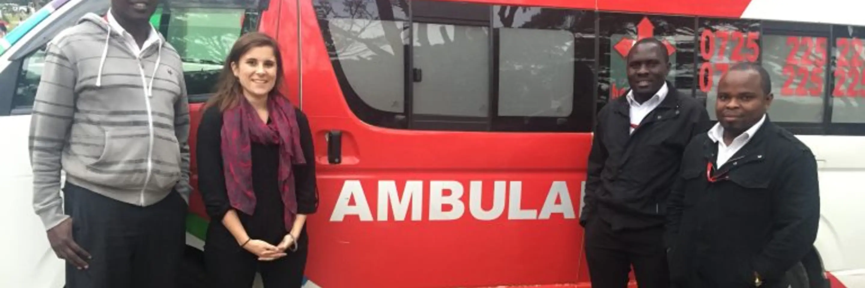 Caitlin Dolkart and three African men standing in front of a red ambulance