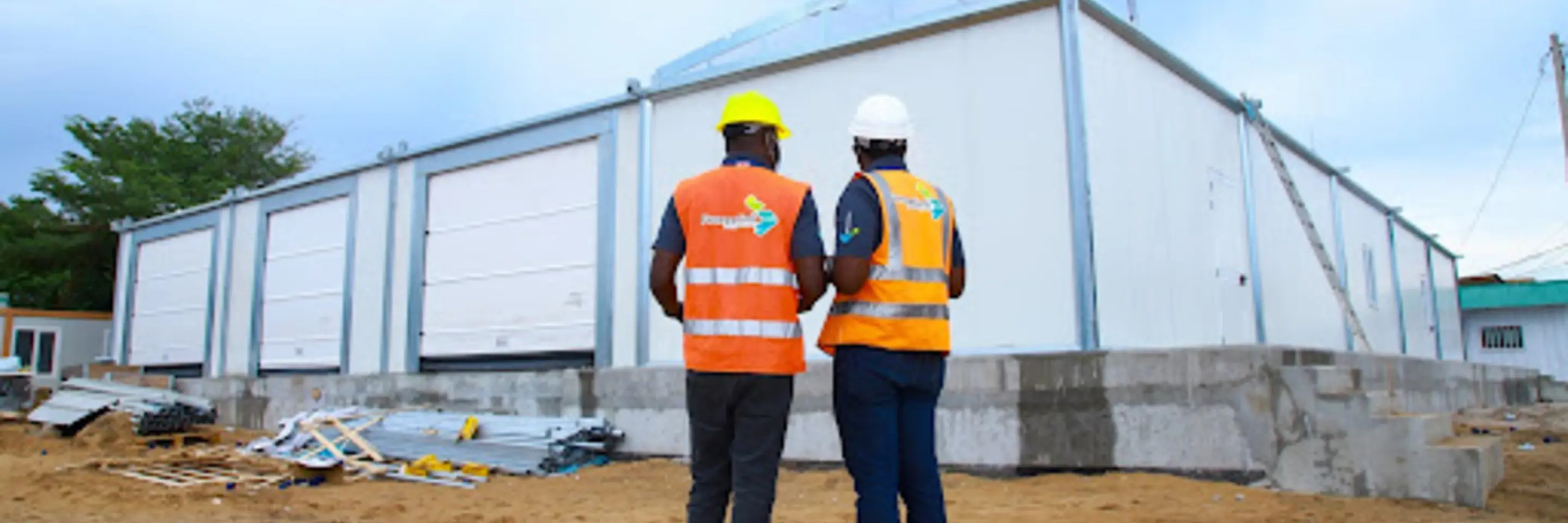 photograph of two men in high-vis vests and hard hats standning infront of a newly built warehouse