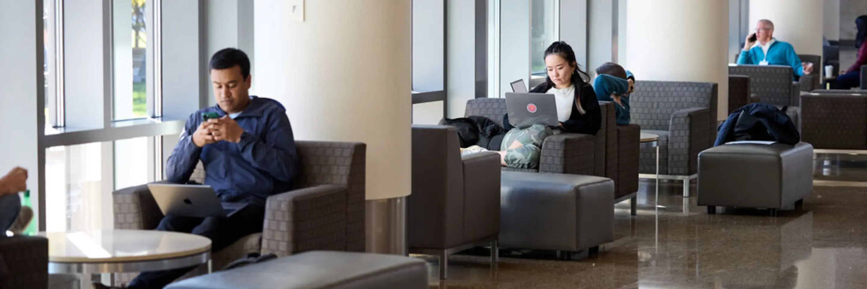 Chairs by the windows near the e62 cafe with a few students sitting and working