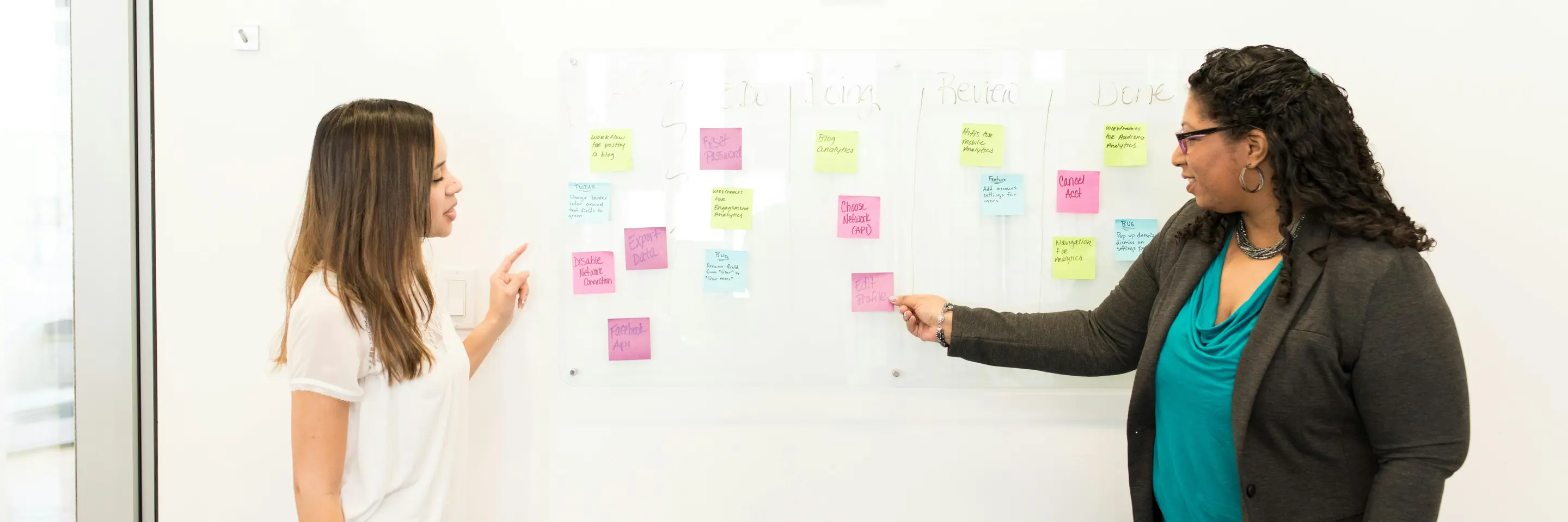 Two women standing in front of a whiteboard with sticky notes on it