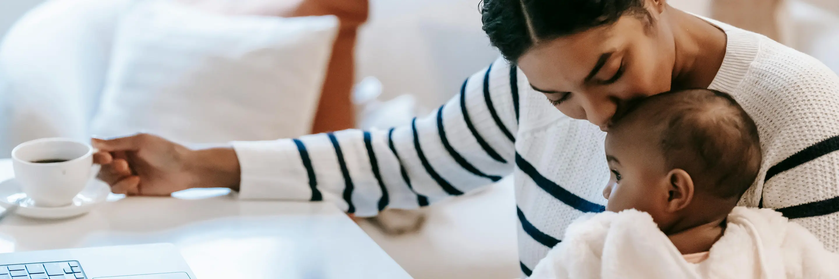 Image of a woman holding a baby in one arm and sitting near a computer