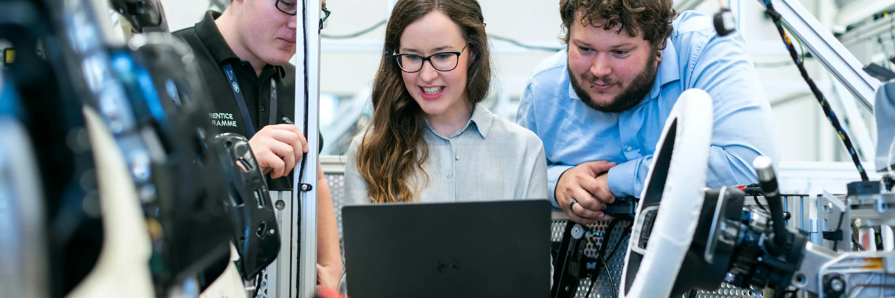 Three people look at a laptop in a some type of industrial setting