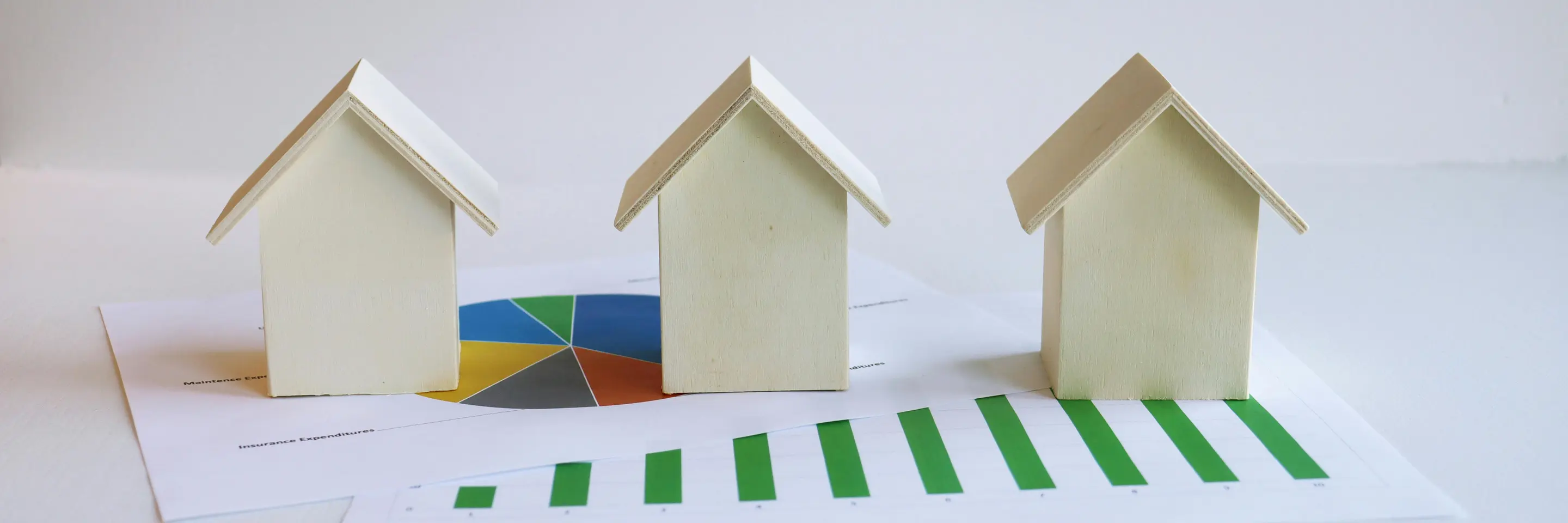 Wooden model houses on graphs depict real estate market analysis and trends.
