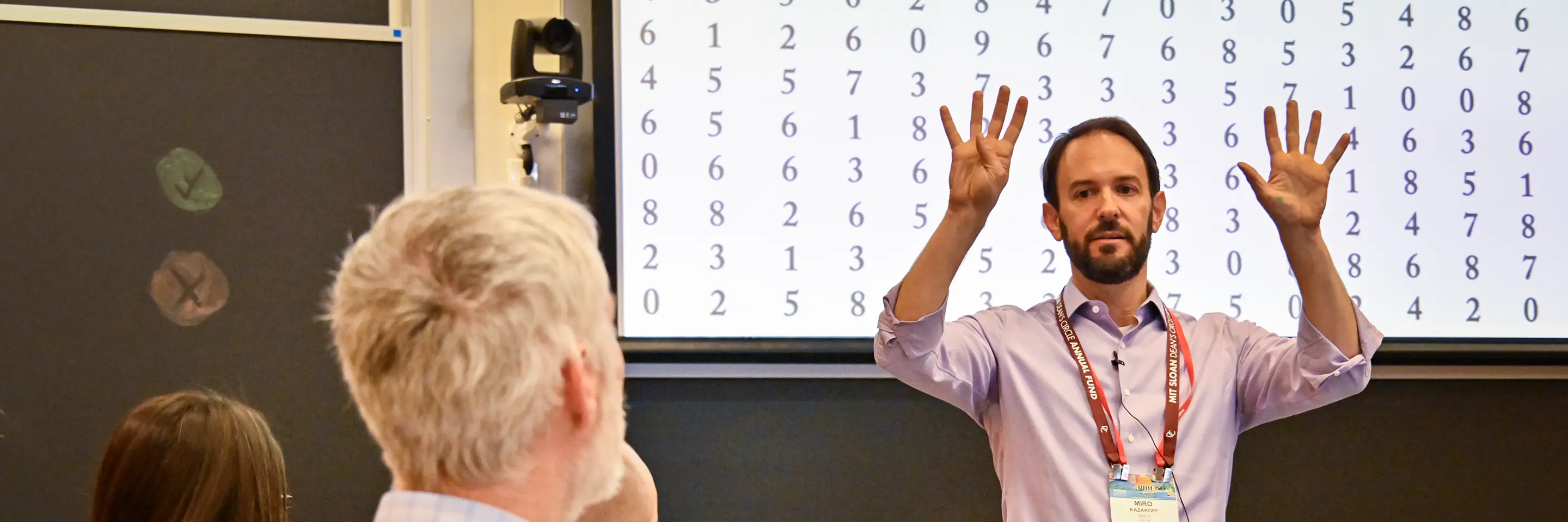 A man gestures while standing in front of a classroom