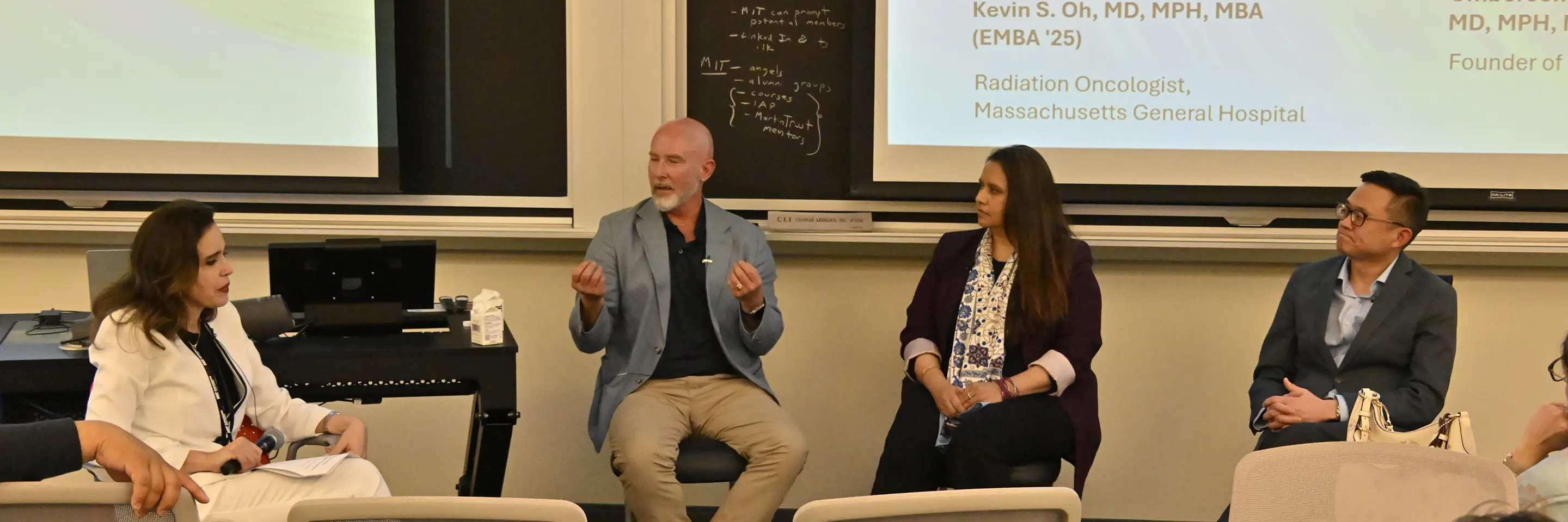 Three people on a panel listen to a fourth panel member speak.