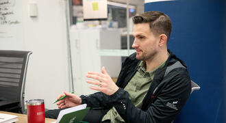 David Brown sits at a desk, talking to someone off camera.