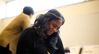 Alecia Asiamigbe looks down at a piece of paper with a pencil in her hand. She sits in an MIT Sloan classroom.
