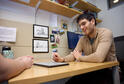 PhD student Ben Manning sits at a desk in the MIT Sloan PhD offices. He looks down at a tablet, talking to someone out of frame.