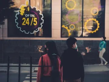 Image of two people with masks standing outside a business with a sign that says "open 24/7"
