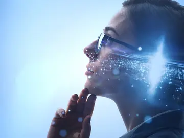 Side view of woman wearing glasses and a bun looking up with fingers on her chin. There is an image of a galaxy overlaid on her head.  