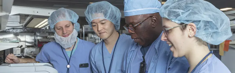 Students and host wearing surgical outfits looking at surgical tools. 