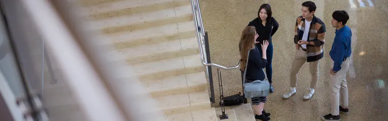 Four MIT Sloan PhD students converse at the bottom of stairs in the MIT Sloan building 