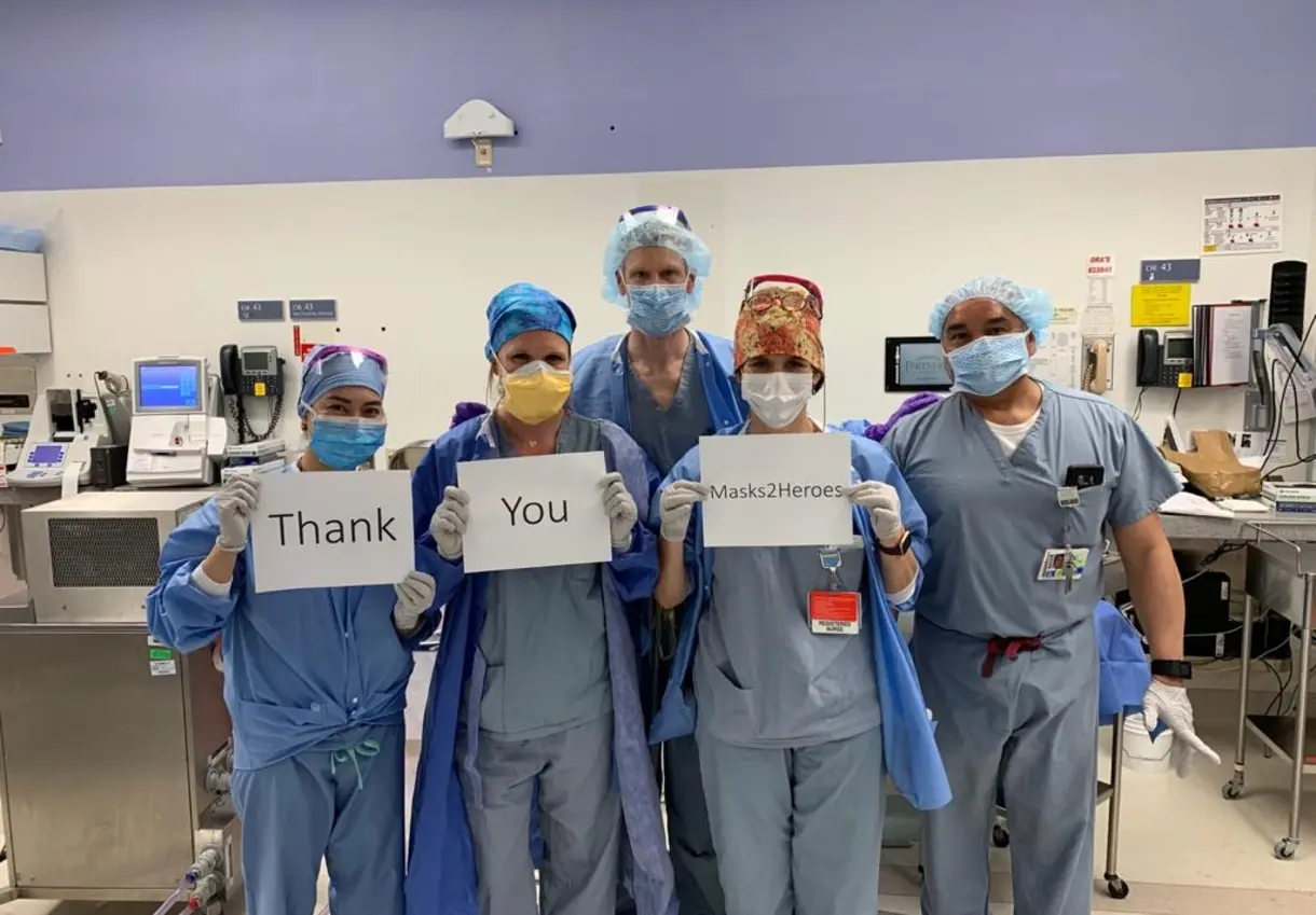 Health care workers with signs reading "Thank you Masks 2 Heroes"