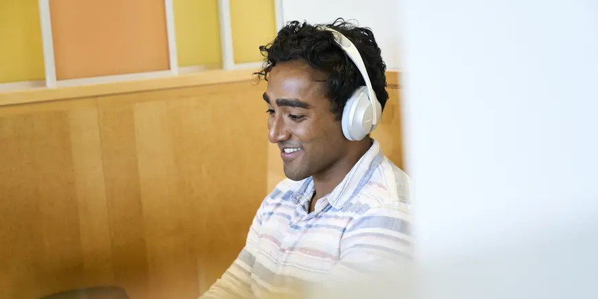 Nikhil, wearing headphones, is smiling while gazing at his laptop