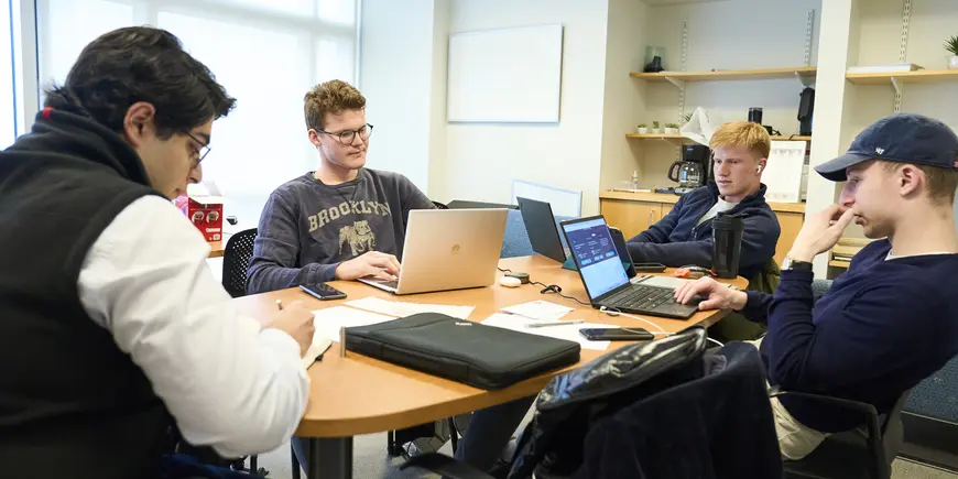 Sandro, William, Alex, and Emil sitting around a table with their laptops in a meeting room