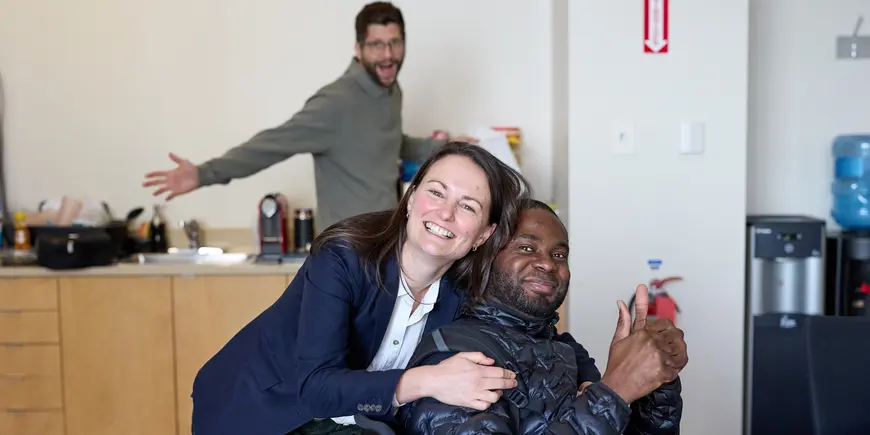 Jocelyn, a student, embraces her friend while another student looks on and smiles.