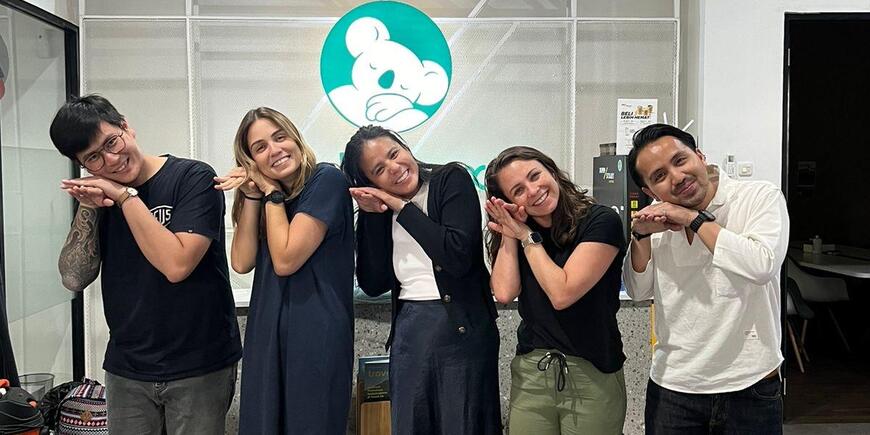 G-Lab team posing, leaning their heads to one side over their hands to imitate Bobobox's logo, which is a sleeping Koala