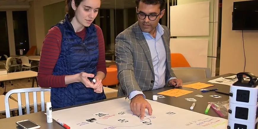 Woman and man look over a table with paper and markers laid out during a business plan meeting