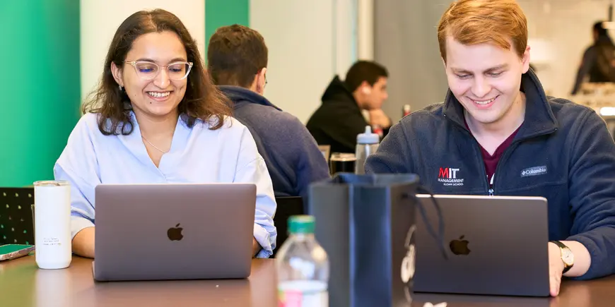 Khushi Pathak and her friend look at their laptops.