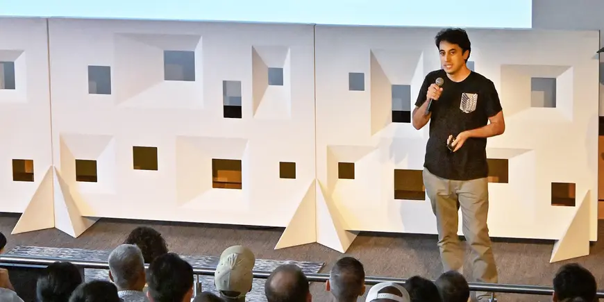 Main in a t-shirt and khaki pants presenting to an audience.