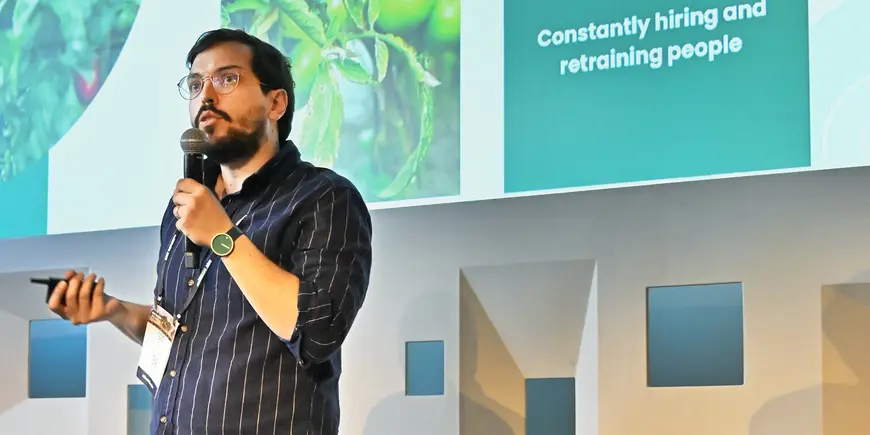 Main in a striped shirt holding a microphone while addressing an audience.