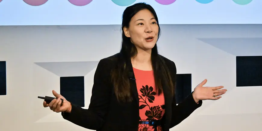 Woman in a black blazer addressing an audience.