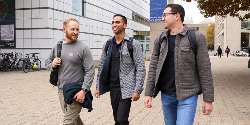 LGO student walks through the MIT campus, talking with two other students.