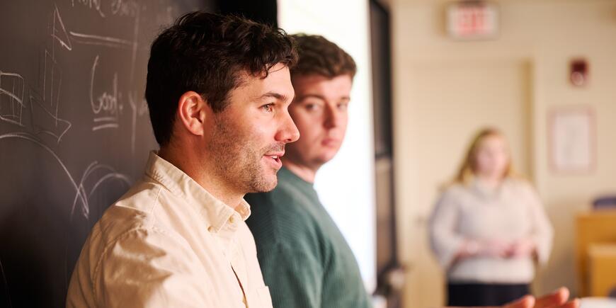 Two men stand in front of a chalkboard and discuss interview tips. 
