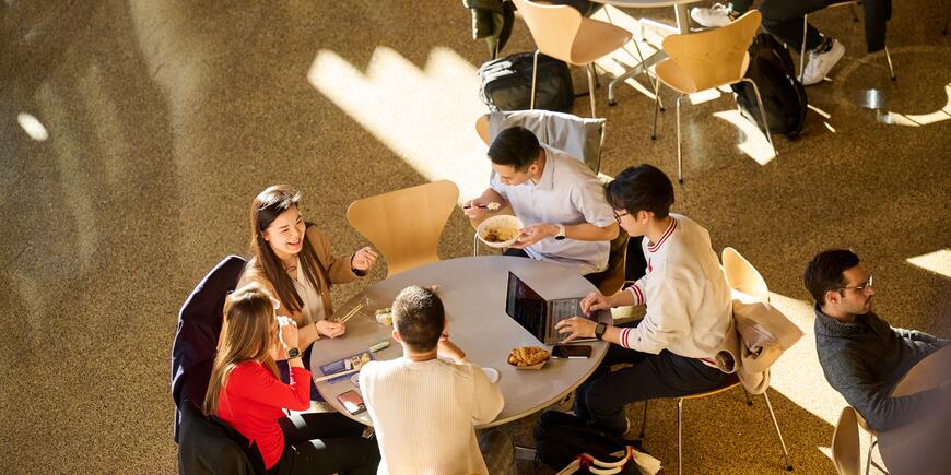 MBA student Sharon Fan sits at a round table eating lunch with other students in the MIT Sloan Cafe.