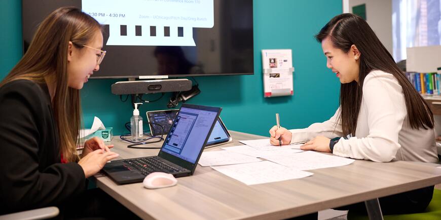 MBA students Sharon Fan and Gloria Wu work together over papers and a laptop.