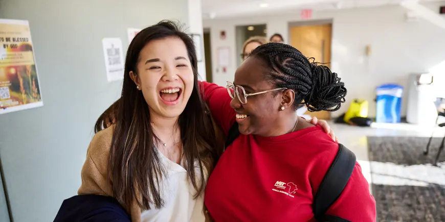 MBA students Sharon Fan and Muele Wilcox hug while walking down a hallway.