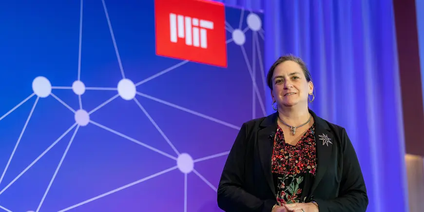 Speaker addresses audience in front of event stage backdrop
