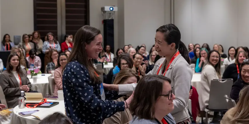 Two smiling women embrace in packed room