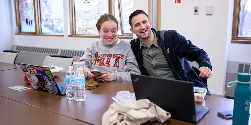 David Brown smiles at the camera with his arm around another MIT Sloan student