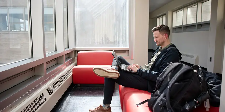 David Brown works on a laptop while sitting on a couch on the skybridge between the Tang Center and the Morris and Sophie Chang Building