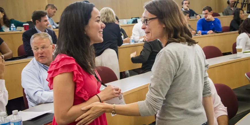 Two women embrace in classroom full of people