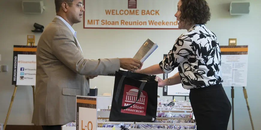 A man speaks with a woman while accepting conference materials from her