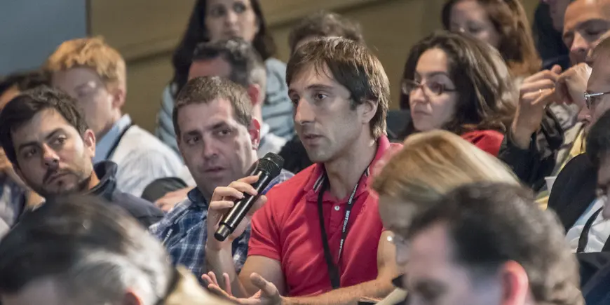 A man with a microphone asks a question in an auditorium full of people