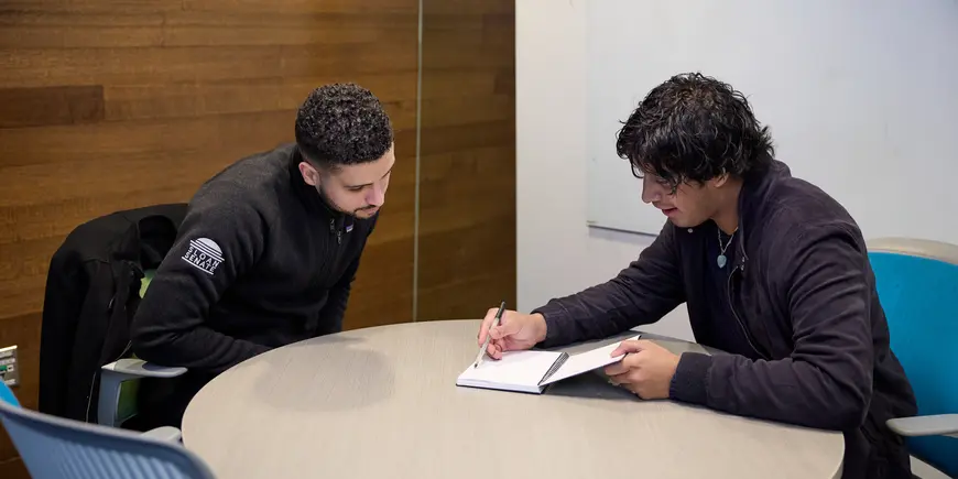 Mike Sanchez sits across a table from a prospective MIT Sloan student. They're looking at a notebook and conversing.