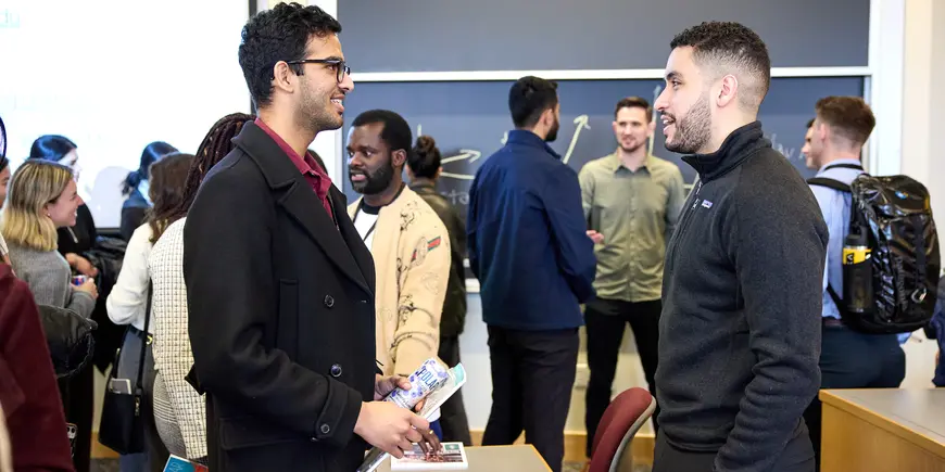Mike Sanchez stands in a room of people. He is talking one-on-one with a prospective student