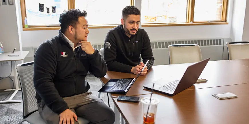 Mike Sanchez and another person take a video conference call. They're in a conference room and looking at a laptop.