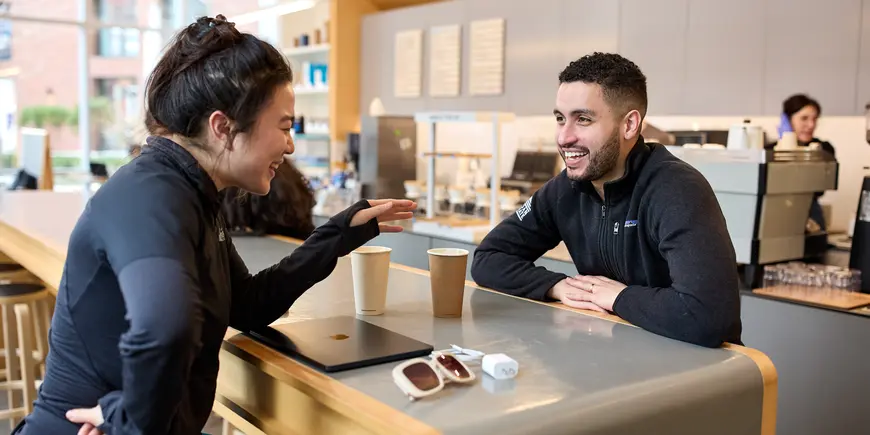Mike Sanchez sits across a table in a cafe from another student. They are chatting and smiling