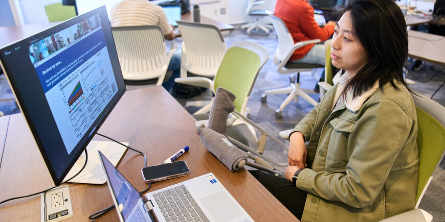 Megan Hung attends a Zoom event. She sits at a desk with a laptop and monitor 