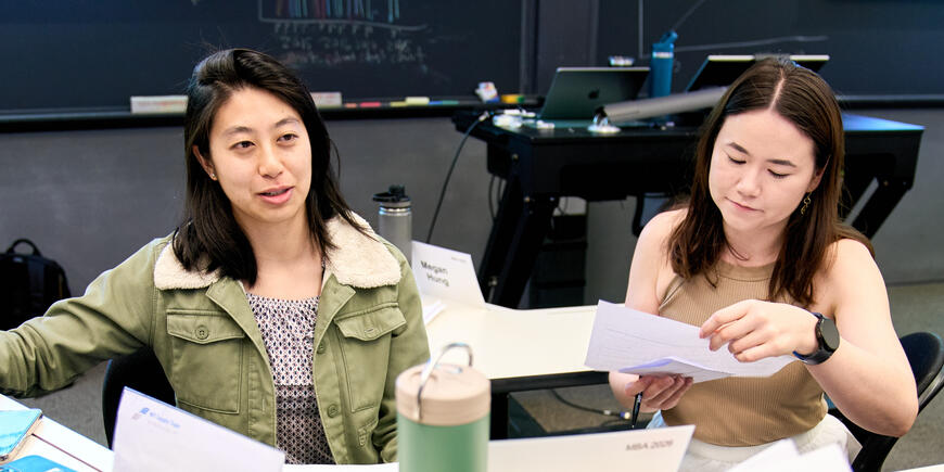 Megan Hung sits with another student, who is looking down at a piece of paper. Megan talks to another person off camera
