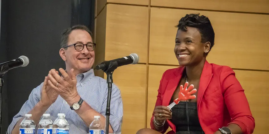 A man claps for a woman sitting next to him on a stage