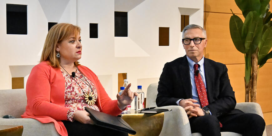 A man listens to a woman presenting in an auditorium
