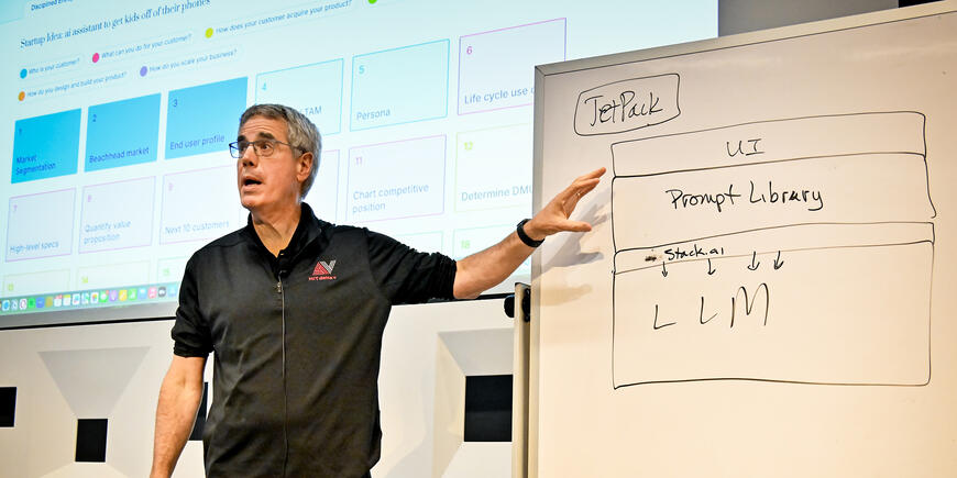 A man gestures at a whiteboard during a presentation