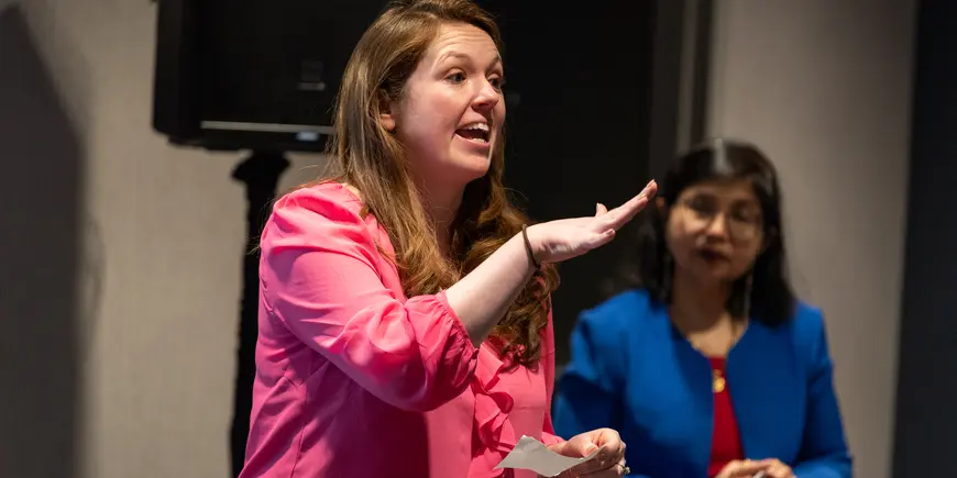 Becca Souza speaking at Hackathon 2023 with Sharmila Chatterjee standing behind her