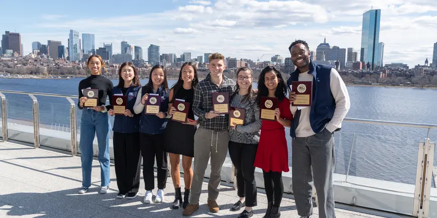 Hackathon 2024 student winners holding their plaques, standing in front of the Charles River